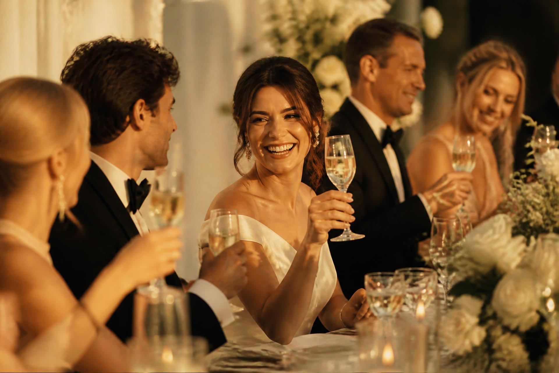 Wedding guests laughing and raising glasses at a candlelit reception